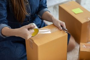 Hands of a woman taping shut a cardboard box